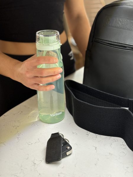 A green water bottle being put in a black bag on top of a counter. Keys are also on the table.